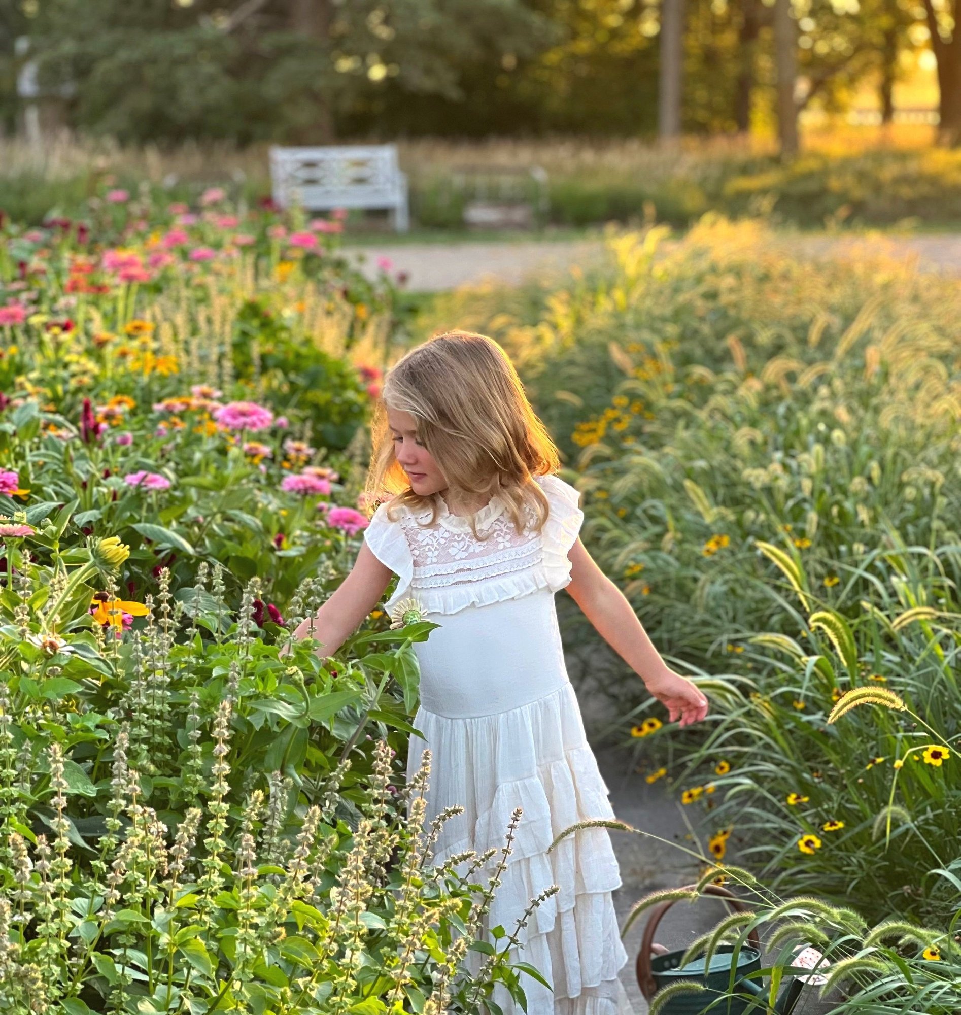 A blonde little girl in a white dress walking between two rows of flowers at Fleurish Flower Farm.
